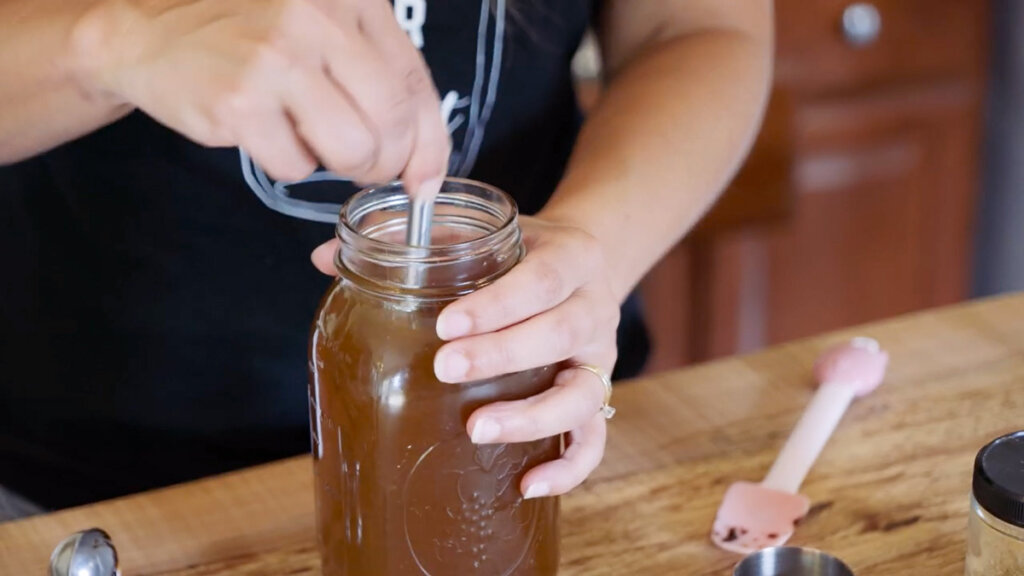 A mason jar of ginger water being stirred to combine.