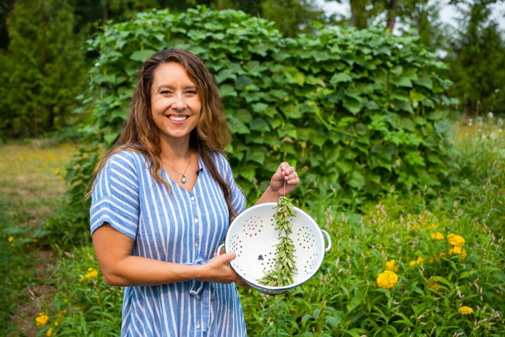 A woman holding up a string of strung green beans that will dry into leather britches.