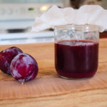 Fruit vinegar in a jar with two plums next to it on the counter.