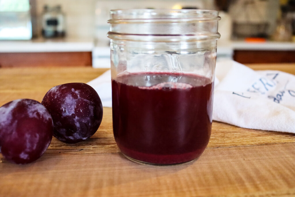 Fruit vinegar in a mason jar with two plums on the counter next to it.