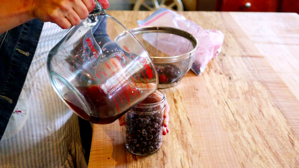 Fruit vinegar being poured over a jar of plums.