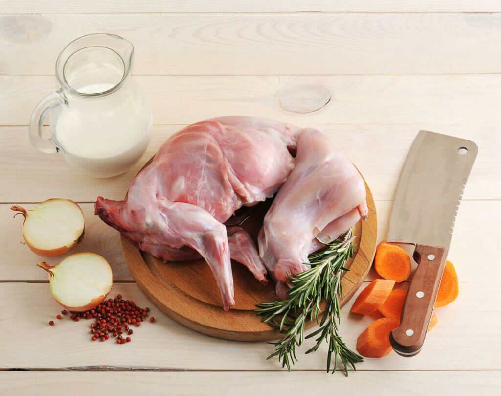 Prepared rabbit on a cutting board with veggies and a butcher knife.