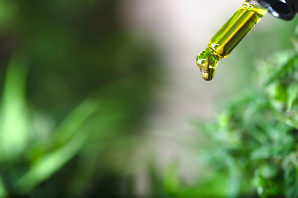 Oil dropping out from a dropper with blurred out plants in the background.