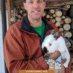 Pinterest pin for raising meat rabbits. Image of a man holding a large rabbit.
