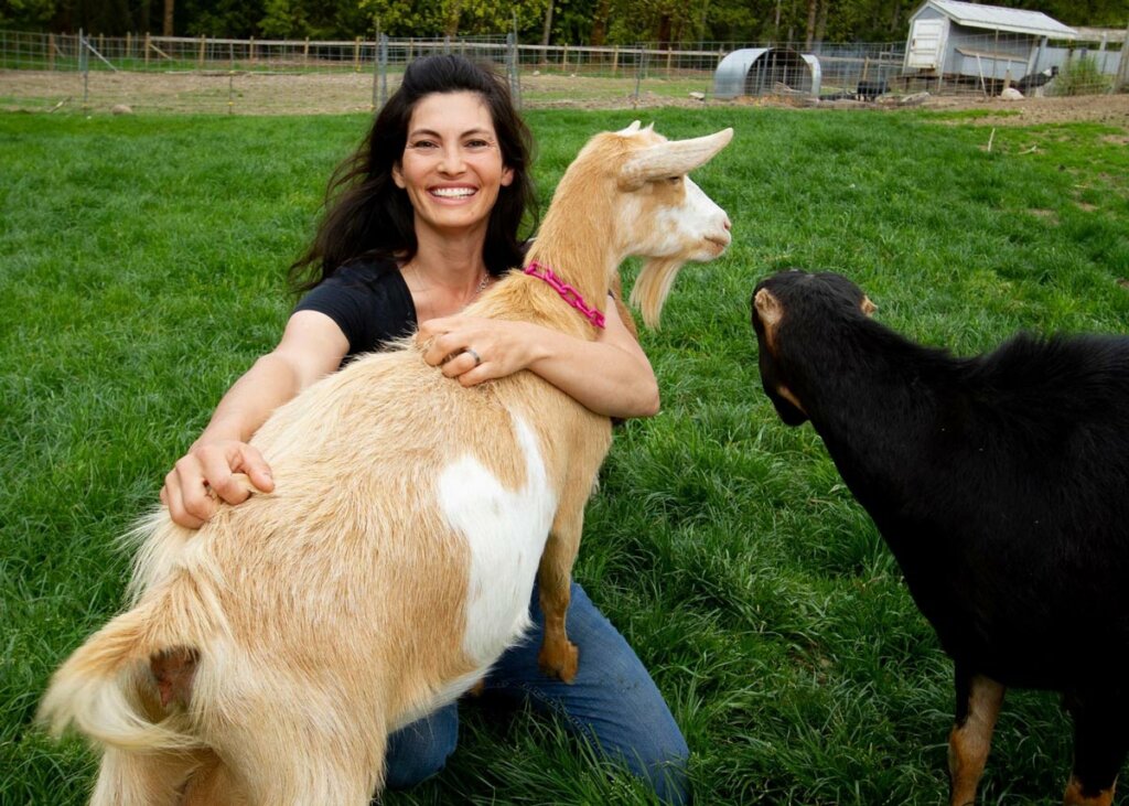 A woman scratching a goat that's in her lap.