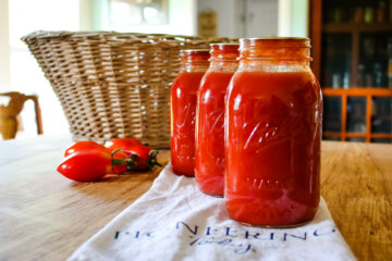 Jars of home canned tomato sauce on counter with ripe paste tomatoes and wicker basket