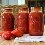 home canned jars of tomato sauce on counter with ripe tomatoes
