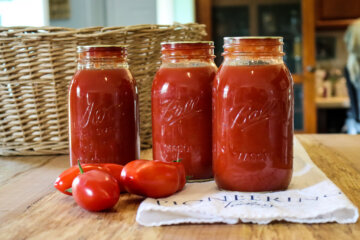 home canned jars of tomato sauce on counter with ripe tomatoes