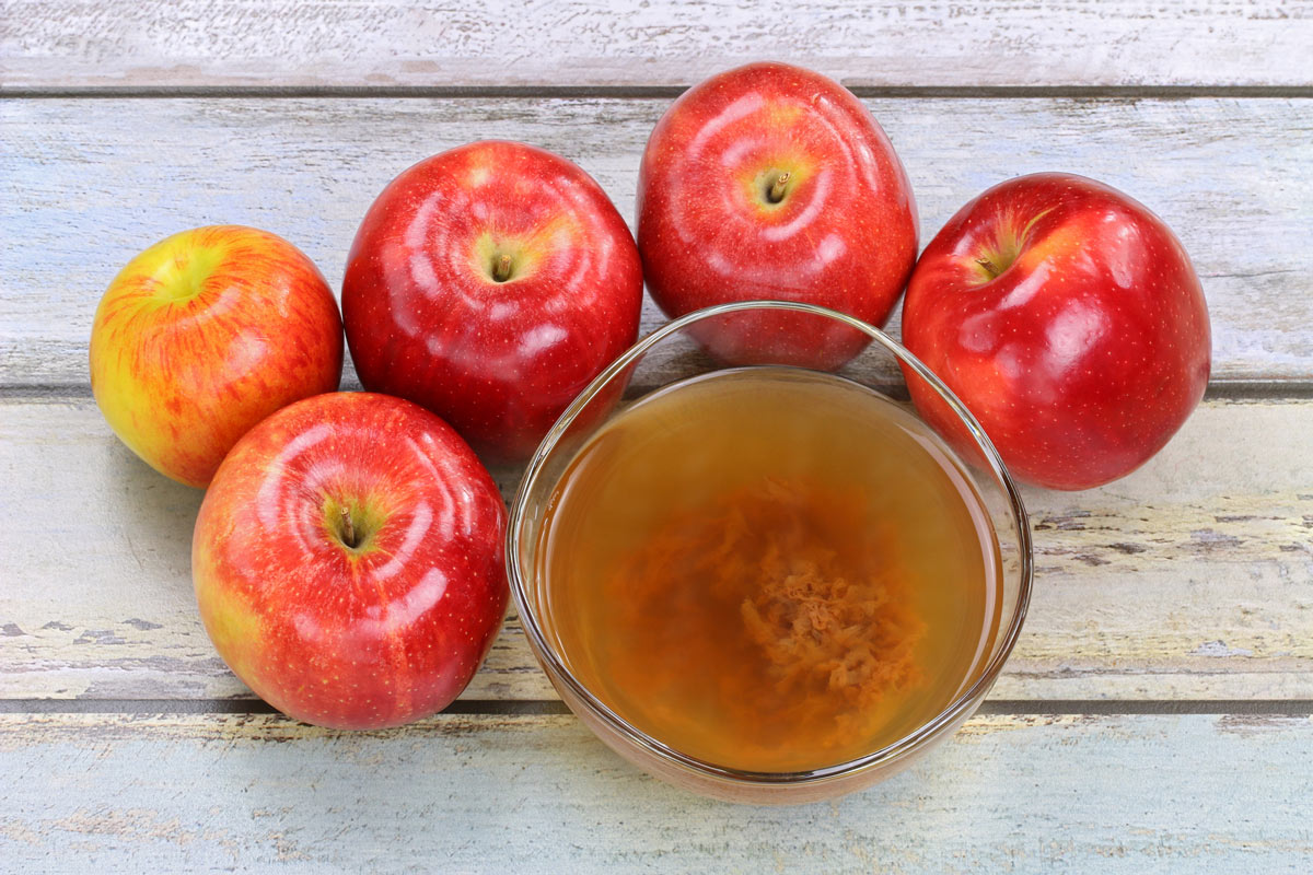 A bowl of homemade apple cider vinegar with the mother next to whole apples.