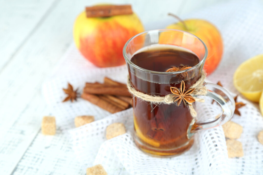 Hot apple cider in a glass with apples and cinnamon around it.