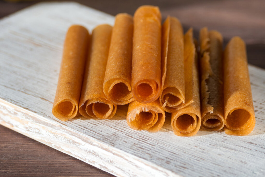 Apple fruit leather rolled up and piled on a white plate.