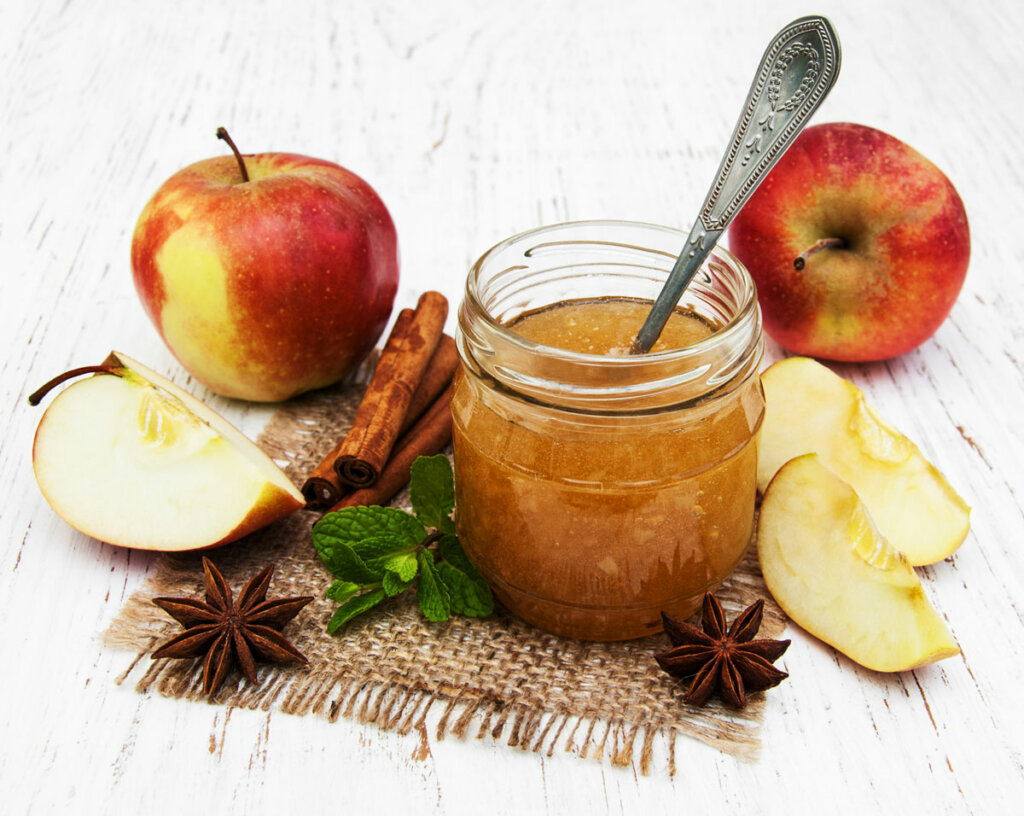 Apple Jelly in a jar with spoon. Apples, cinnamon sticks and star anise around it.