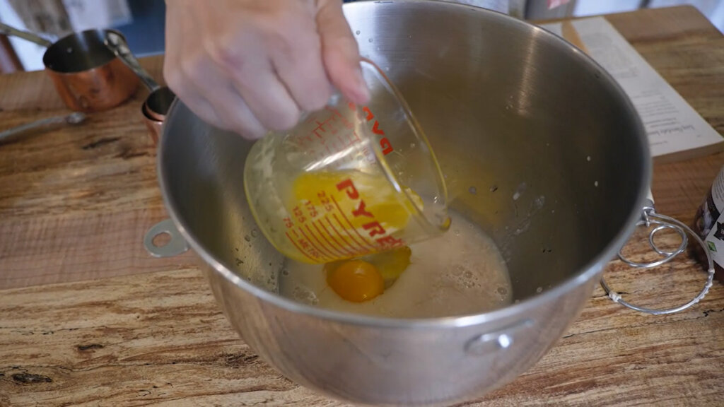 Melted butter being poured into a mixing bowl that has water, yeast, and an egg.