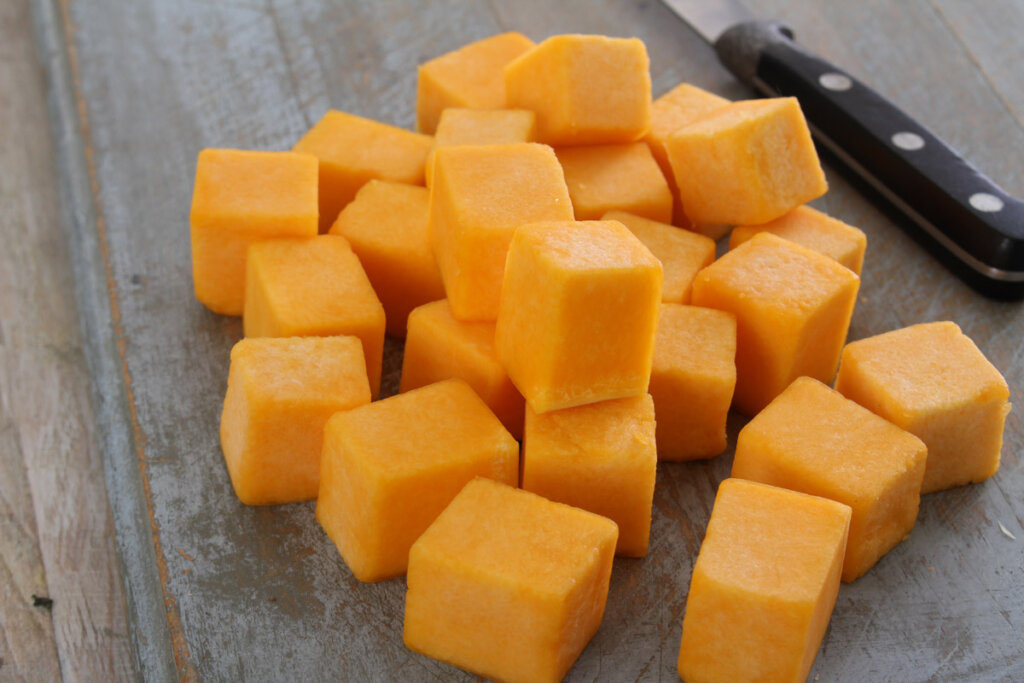 Cubed pumpkin on a wooden table with cutting knife to the side.