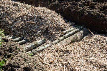 A hugelkultur bed in the ground with layers of logs and wood chips.