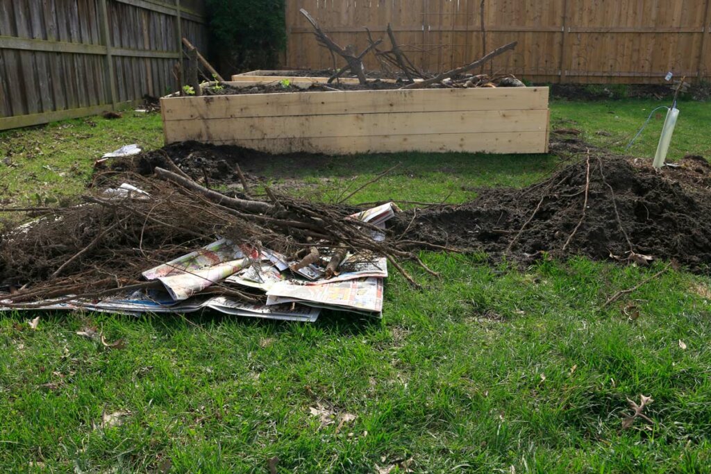 Supplies needed for a hugelkultur bed. Piles of branches, wood chips, newspaper.