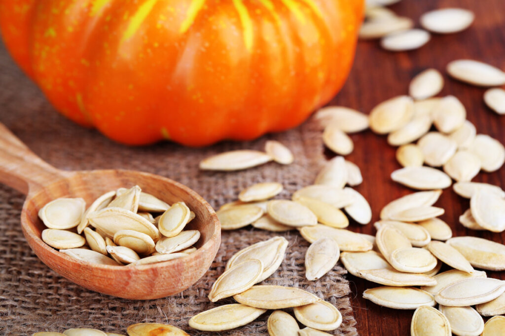 A pumpkin with dried pumpkin seeds spread on a table.