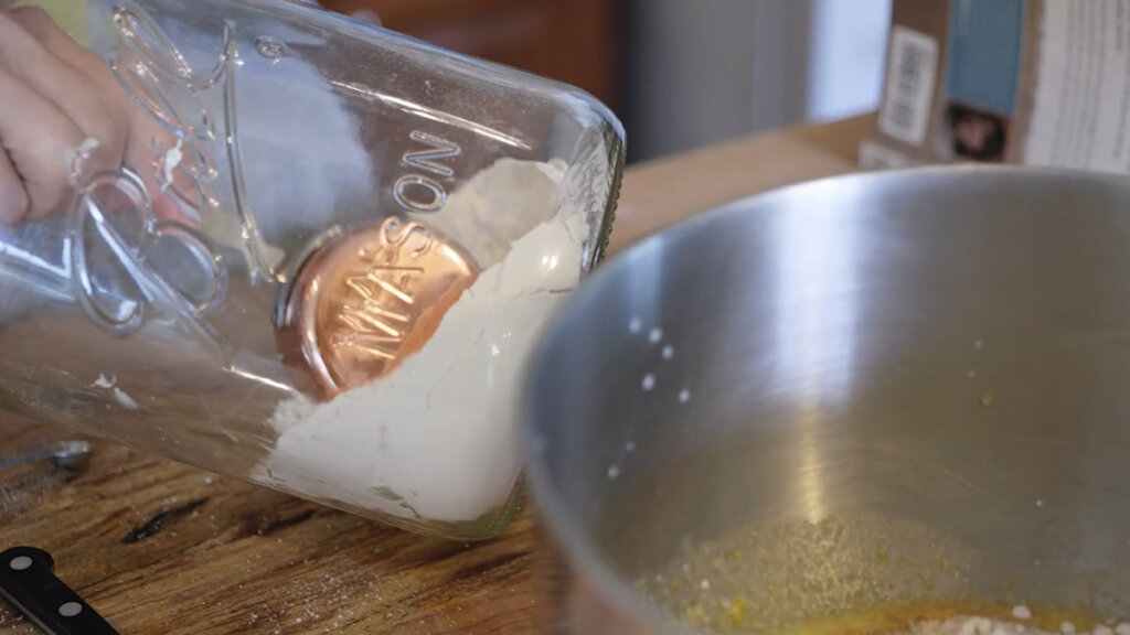 A measuring cup inside a large mason jar getting a scoop of flour.