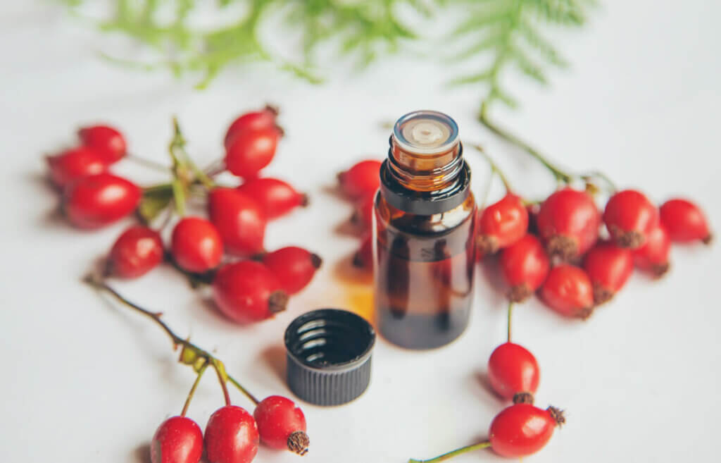 Rosehips on a counter next to a bottle of rosehip essential oil.