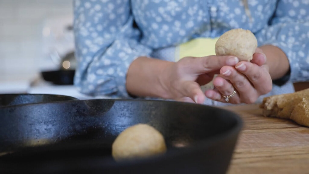 A woman's hands forming rolls with a cast iron pan of rolls in the forefront.