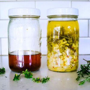 Two mason jars sitting on a counter. One with fire cider ingredients steeping in a jar, another jar with completed fire cider.