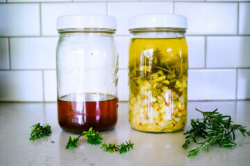 Two mason jars sitting on a counter. One with fire cider ingredients steeping in a jar, another jar with completed fire cider.