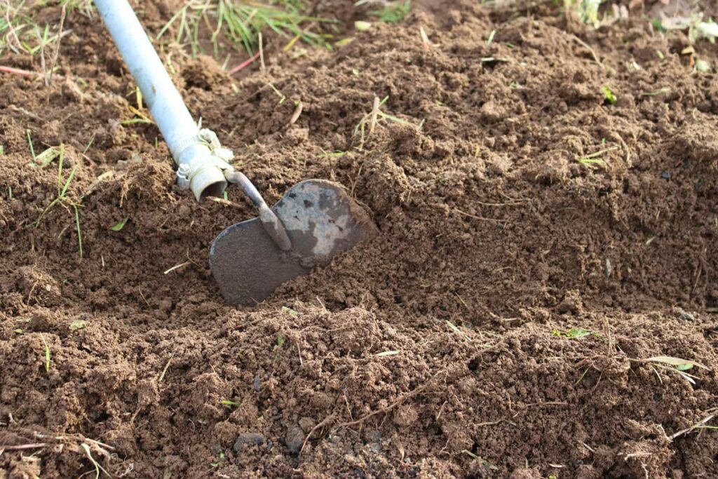 A hoe digging a trench in a garden bed.