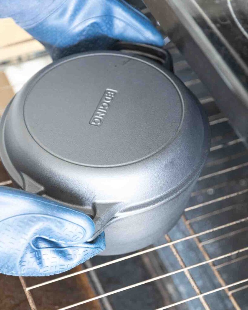 Hands with oven mitts placing a Dutch oven inside a preheated oven.