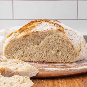 Slices of no-knead artisan bread sitting in front of the rest of the loaf on a wooden cutting board.