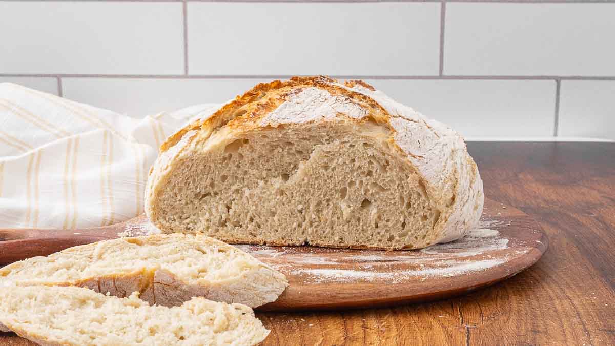 Slices of no-knead artisan bread sitting in front of the rest of the loaf on a wooden cutting board.