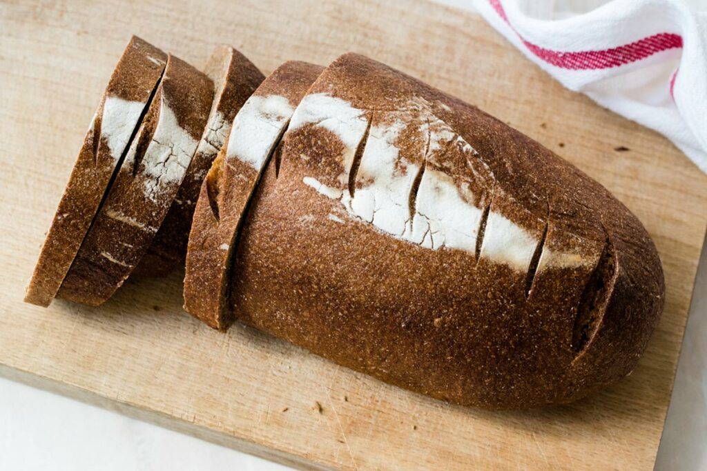 A loaf of einkorn bread sliced on a wooden cutting board.