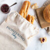 Linen bread bag with two baguettes, cutting board with round loaf of artisan bread, butter and jam on counter top