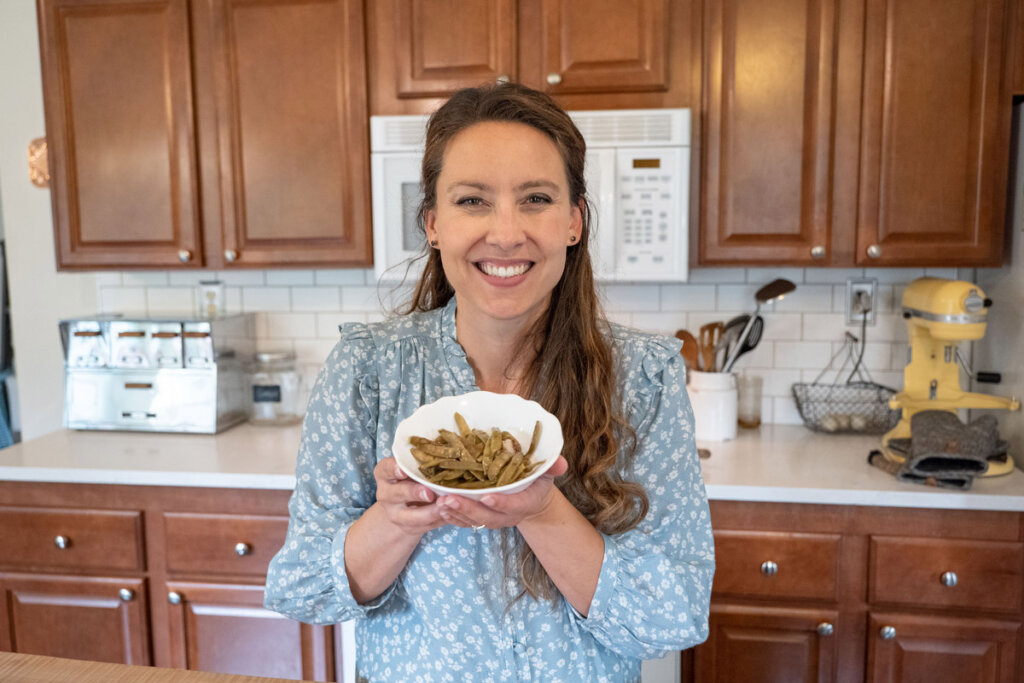 A woman holding a bowl of cooked green beans.