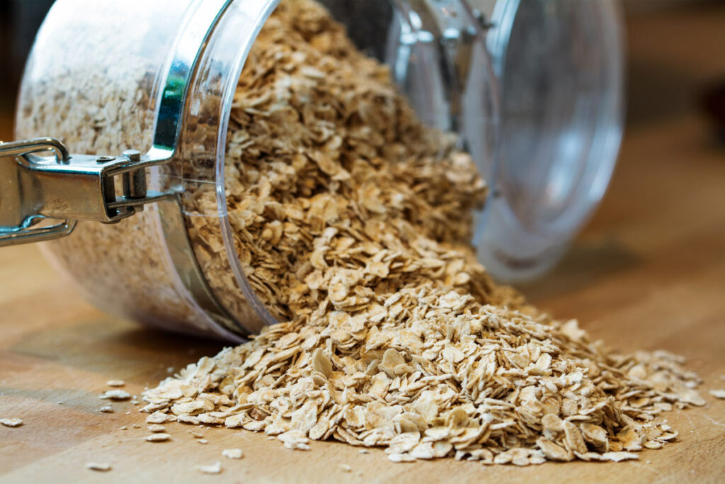 A jar of oats tipped over onto a wooden counter.
