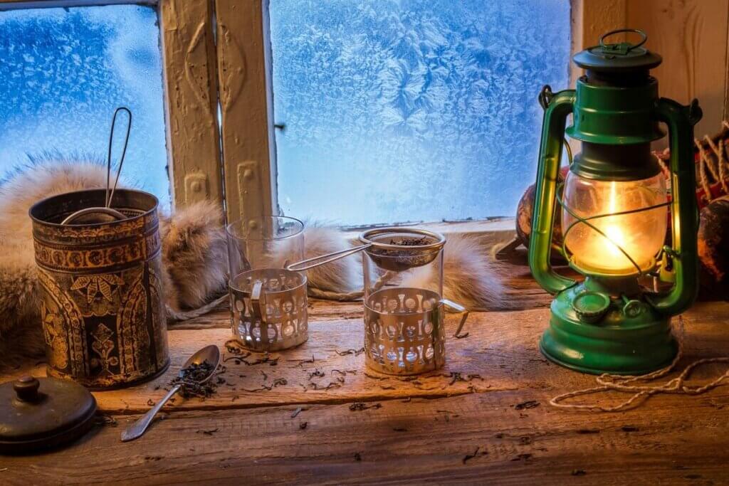 Oil lamp sitting on a wooden table next to a frosted window.