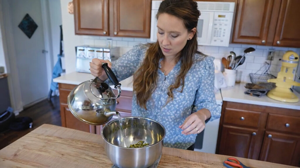 A woman pouring hot water from a kettle into a bowl.