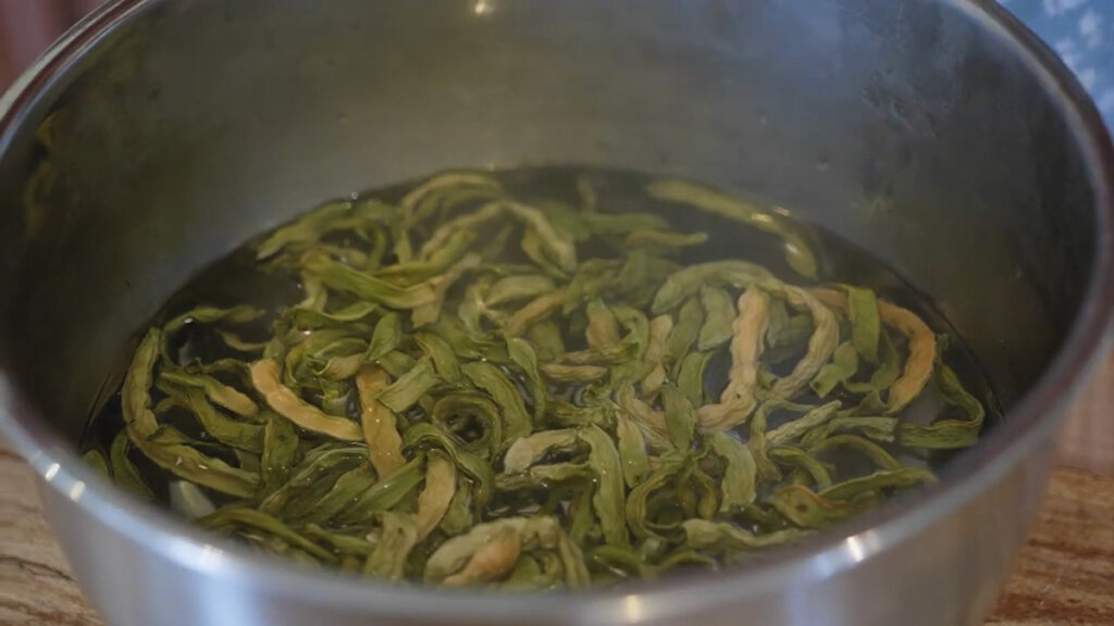 A stainless steel bowl filled with dried green beans covered in boiling water.