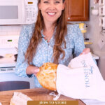 Pinterest pin for how to store bread. Image of a woman putting a loaf of homemade artisan bread into a linen bread bag.