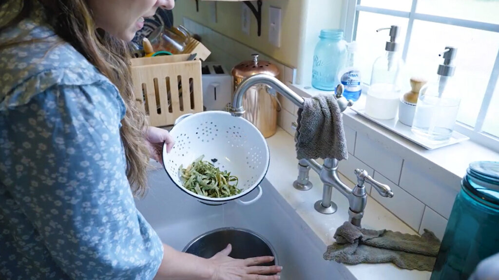 A woman rinsing green beans in a colander in the sink.