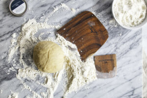 Koa wood bench knife and scraper on counter top with flour and pie dough