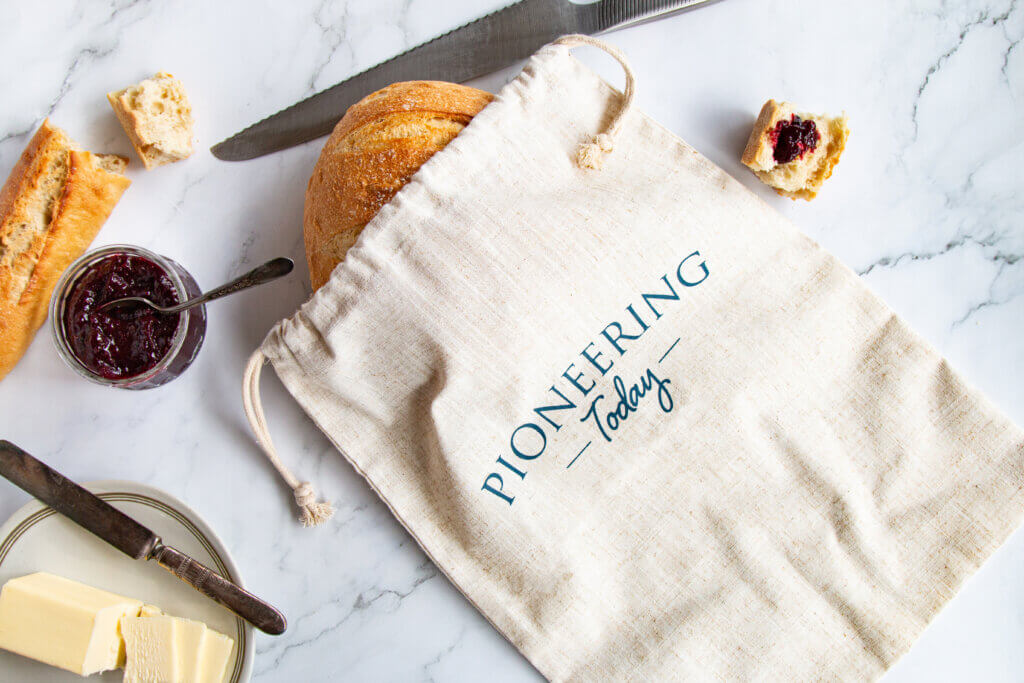 round loaf of bread in linen bread bag on counter with butter and jam