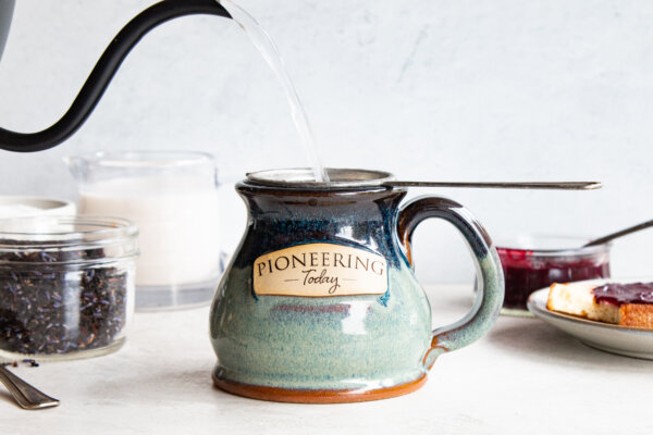 Clay mug with "Pioneering Today" stamped and a tea pot pouring water into the mug.