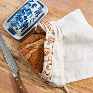 Sliced loaf staying fresh in a USA-made beeswax-lined organic cotton Pioneering Today bread bag on a wood cutting board.