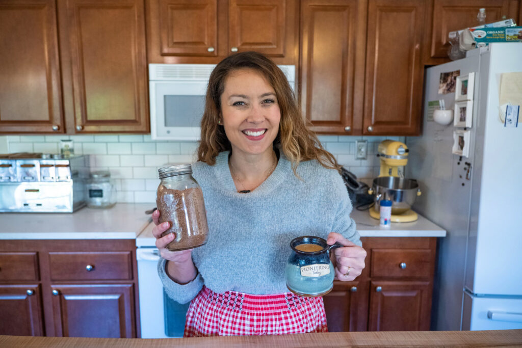 A woman holding a jar of freeze dried hot cocoa mix and a mug of hot cocoa.