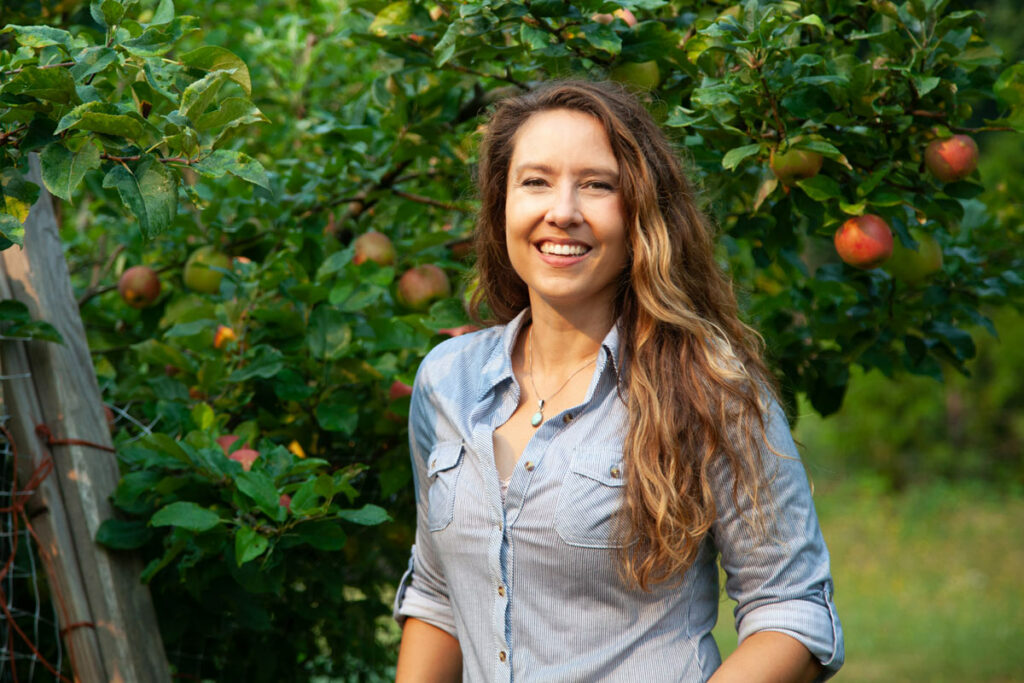 A woman standing in an apple orchard.