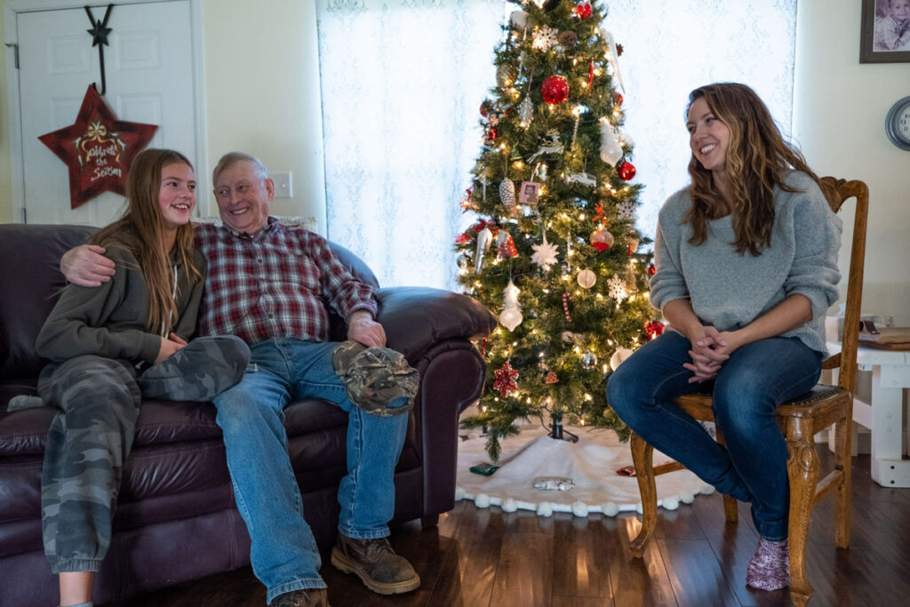 A grandfather, mother and daughter sitting around a Christmas tree.