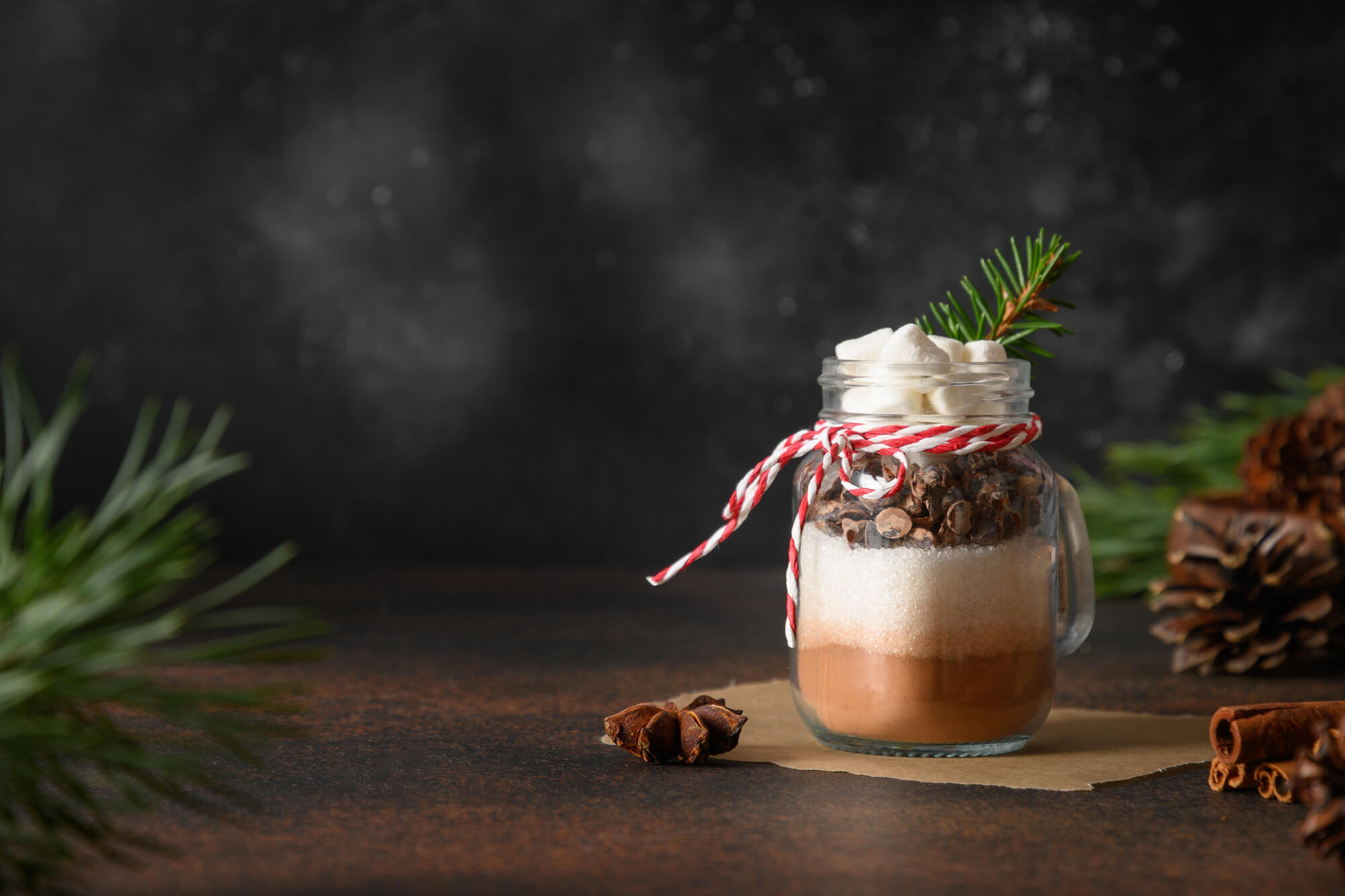 homemade hot cocoa mix in a mason jar with red and white twine and pine cones on table top