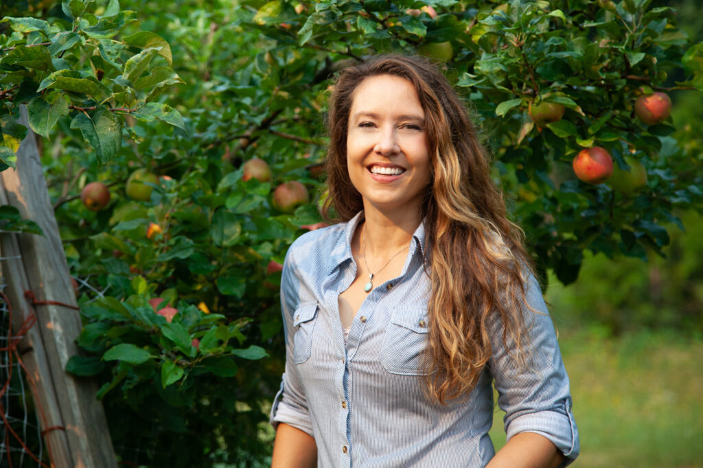 A woman standing in front of an apple tree.