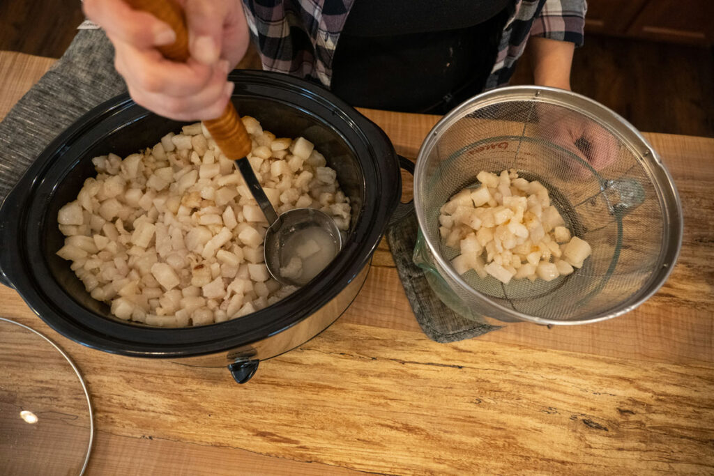 A woman ladling lard into a strainer to catch the liquid rendering.