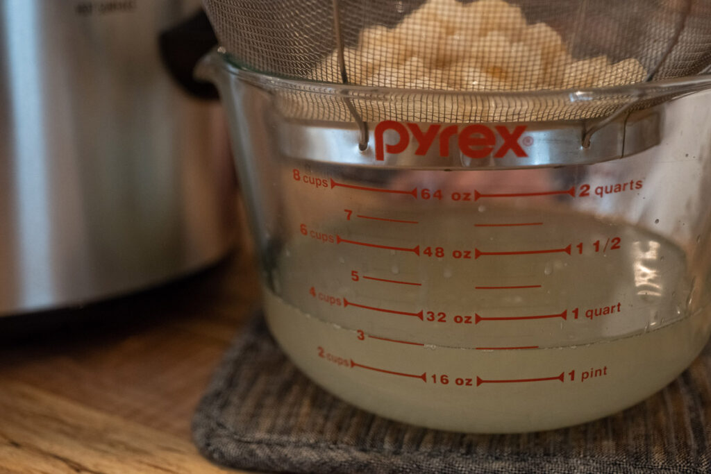 Lard pieces straining into a large bowl through a metal colander.